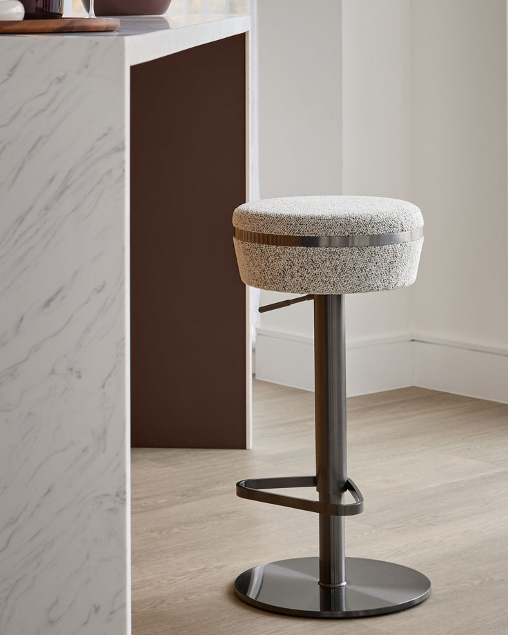 Kian gas lift bar stool in grey fabric with dark bronze metal base and footrest, shown in modern kitchen setting.