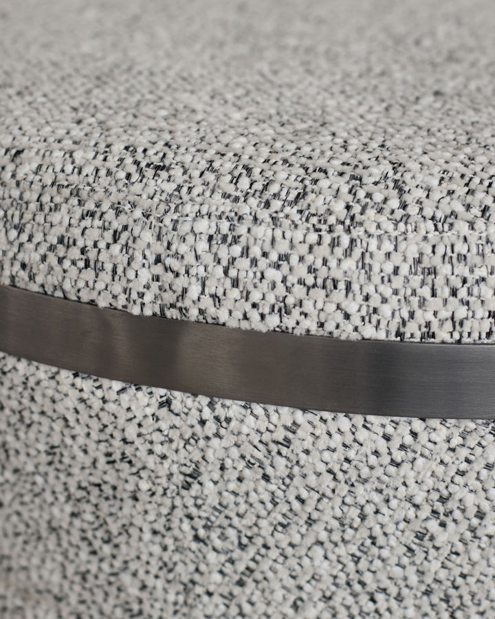 Grey upholstered fabric with black metal band detail, close-up view showing texture.