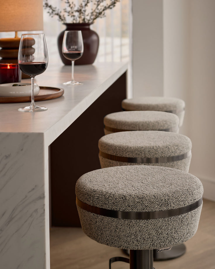 Kian grey fabric gas lift bar stools with black metal bands, lined up at a marble counter in a modern kitchen setting.