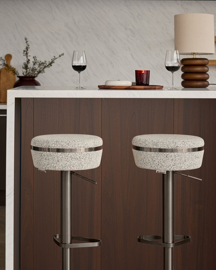 Kian gas lift bar stools with grey textured fabric seats, stainless steel bases, and metal footrests positioned at a kitchen counter.