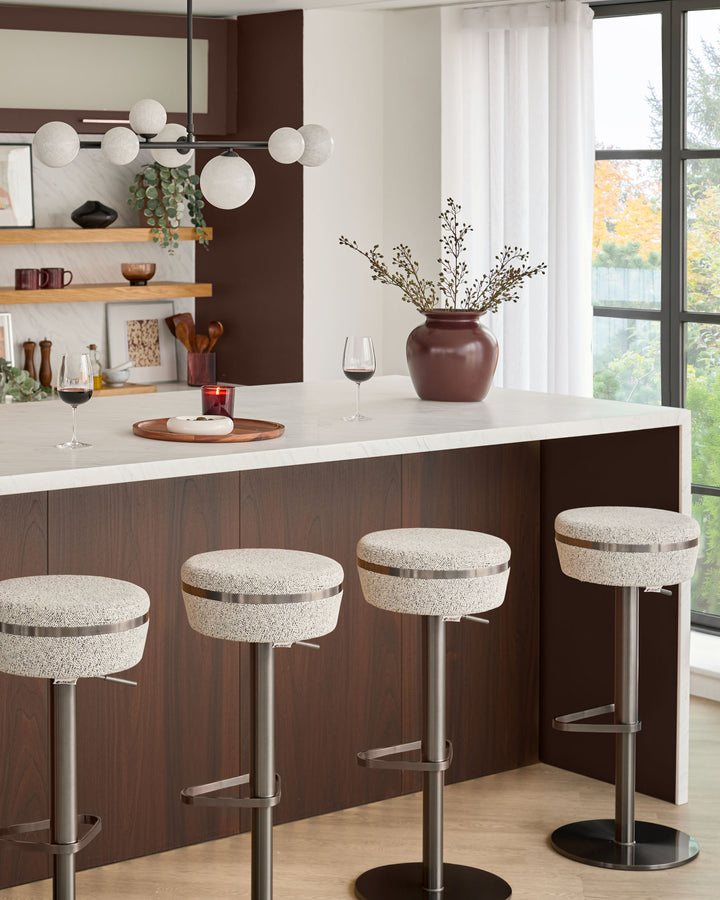 Kian gas lift bar stools with beige upholstery, brushed metal stems, and black round bases positioned at a dark wood kitchen island.