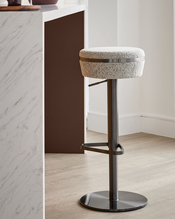 Kian grey fabric gas lift bar stool with dark metal base and footrest, shown in modern kitchen setting.