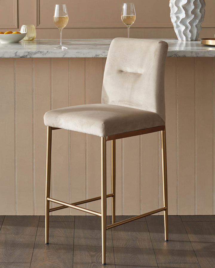 A stylish, tall, light-beige stool with gold legs sits on a wooden floor. Above, on a marble countertop, are drinks.