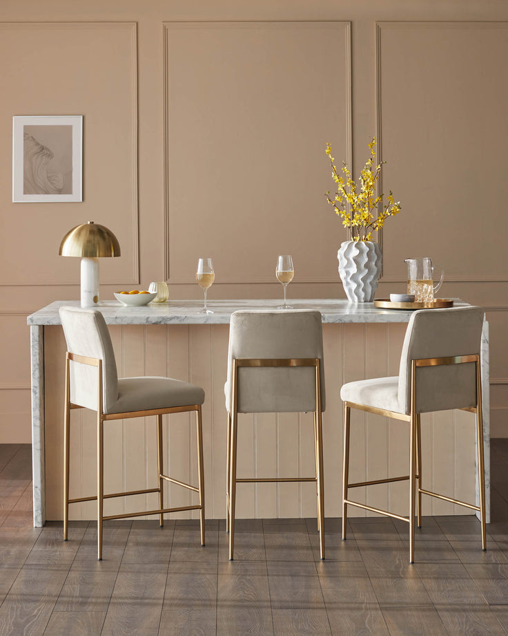 Stylish bar stools with gold frames and neutral upholstery at a marble counter.