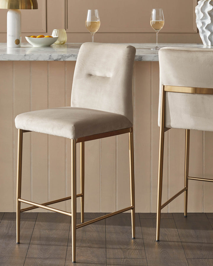 Two elegant bar stools with gold frames and light velvet seats sit at a marble-topped bar, exuding sophistication.