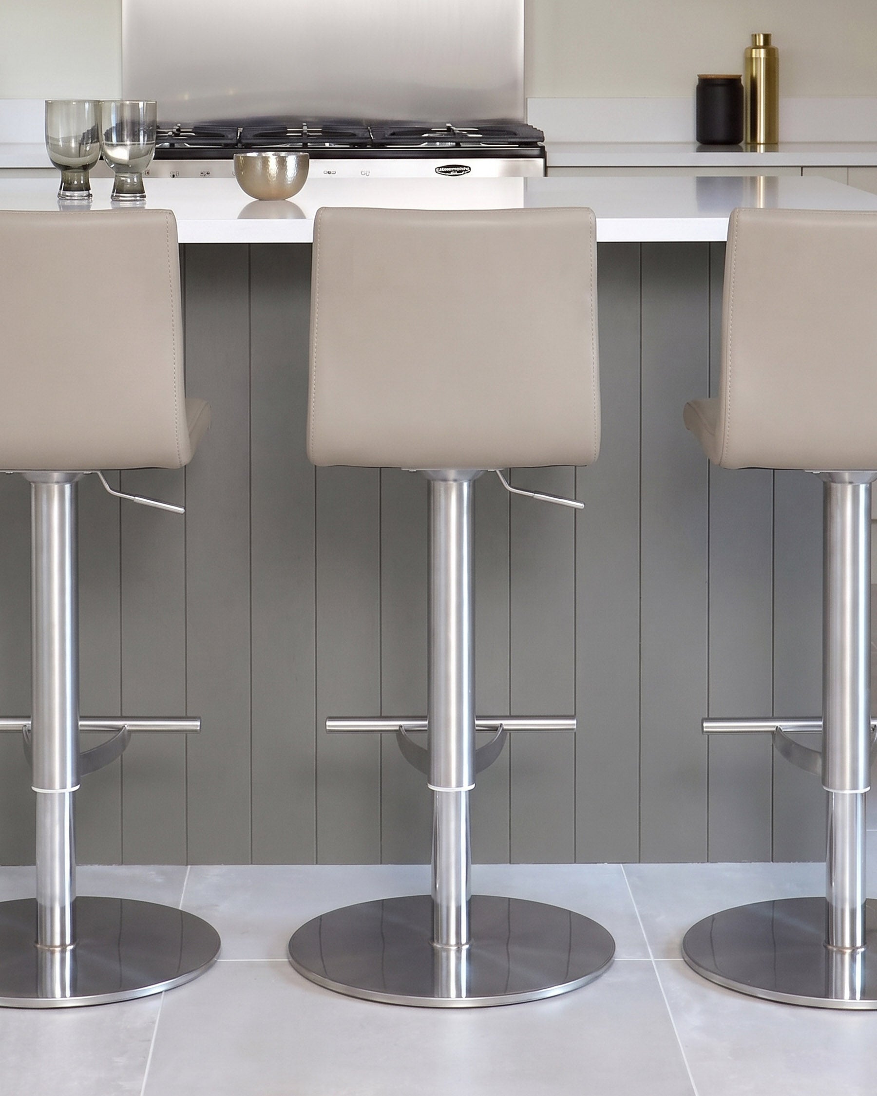 Kiki light grey real leather gas-lift bar stools with brushed stainless steel bases, shown in modern kitchen setting.