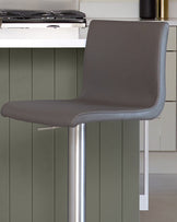 Dark grey leather gas lift bar stool with curved backrest and polished chrome base, shown in kitchen setting.
