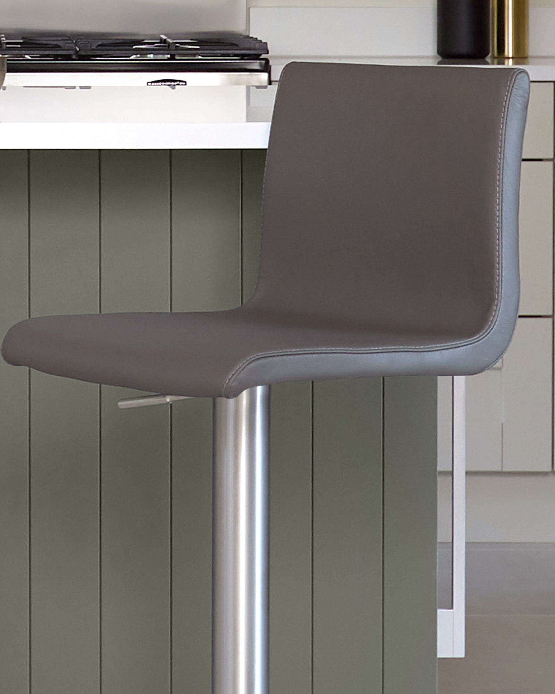 Dark grey leather gas lift bar stool with curved backrest and polished chrome base, shown in kitchen setting.