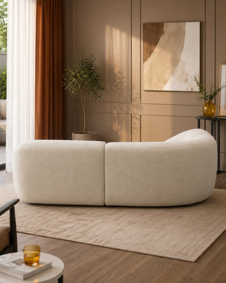Kimberley square corner sofa in natural fabric, curved design, shown in modern living room setting with warm lighting.