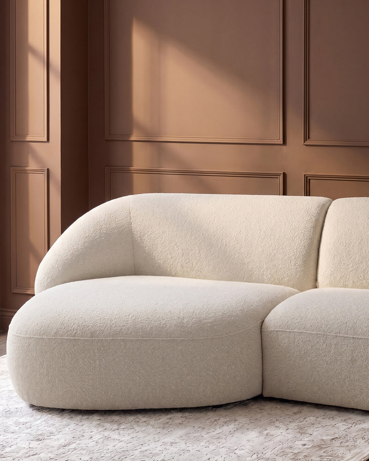 Kimberley left-hand chaise 3-seater sofa in natural fabric with curved, rounded design against paneled wall.