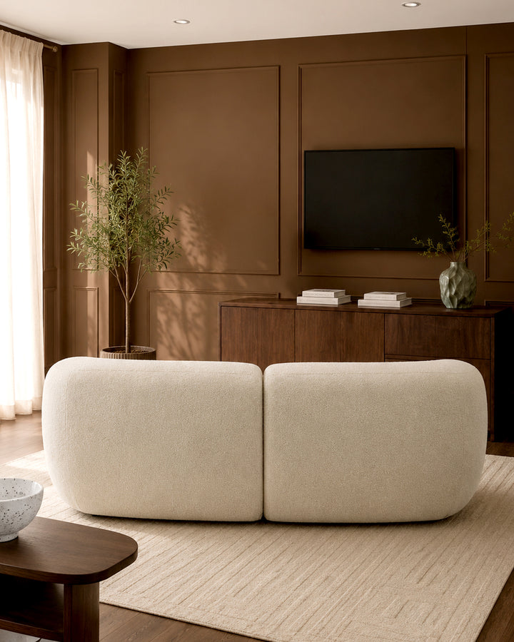 Kimberley 3-seater sofa in natural fabric with rounded, cushioned design, shown in a warm brown living room setting.