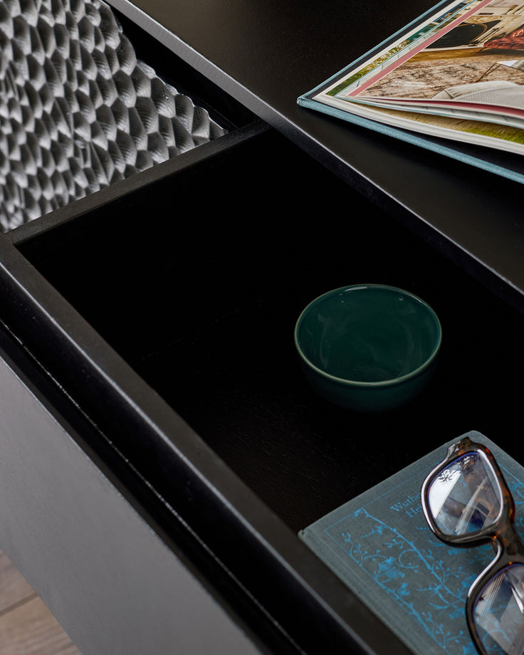 Black wooden sideboard with open drawer displaying interior storage, styled with decorative items including a green bowl and eyeglasses.