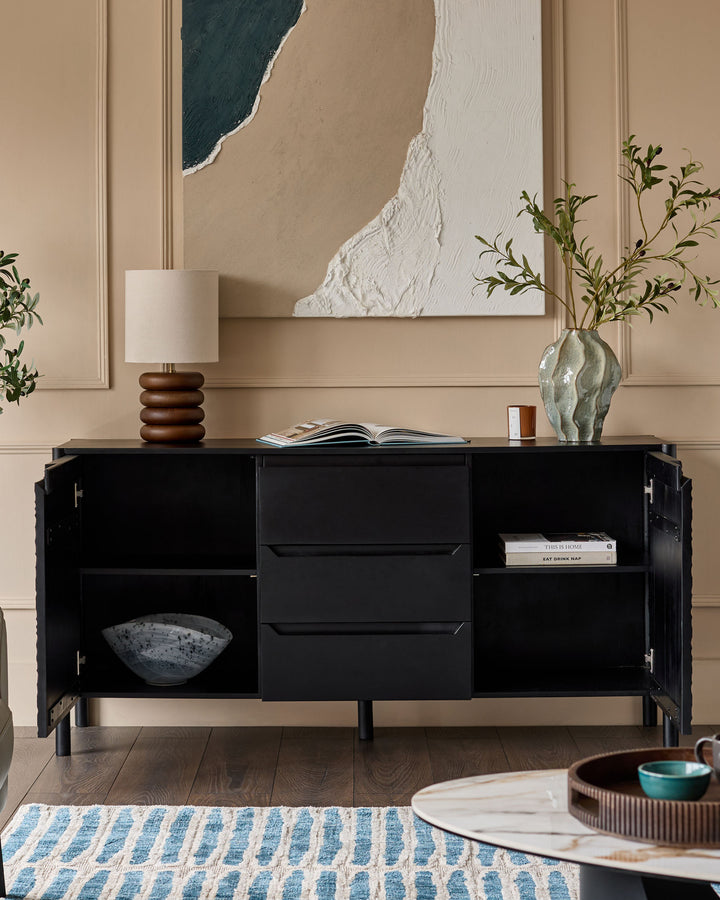 Black wood sideboard with open cabinet doors, drawers, and shelving displaying decorative items in a neutral beige room.