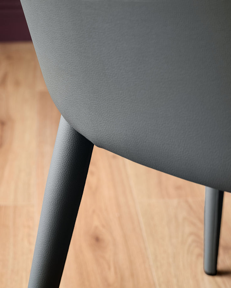 Dark grey faux leather dining chair with black legs, shown at an angle on a wooden floor.