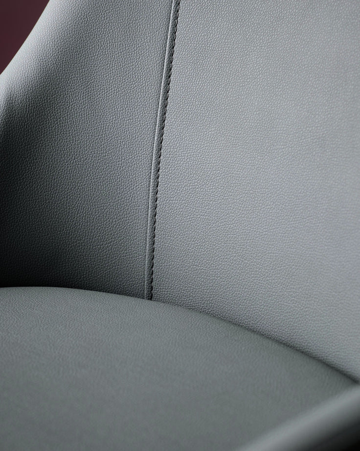 Close-up of dark grey faux leather dining chair showing textured upholstery and center seam detail.
