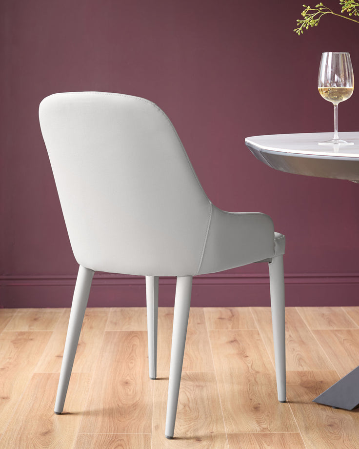 Light grey faux leather dining chair with curved backrest and tapered legs, shown from rear angle at a dining table.