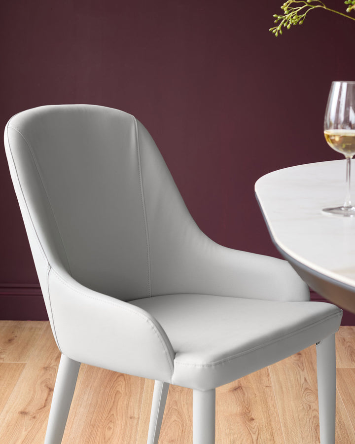 Light grey faux leather dining chair with curved backrest and tapered legs, positioned at a round white table with wine glass.