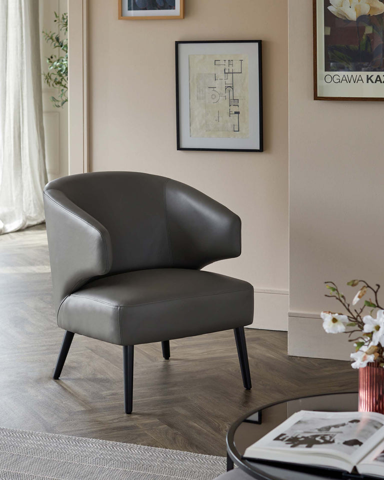Modern grey upholstered accent chair with a curved backrest and seat, featuring sleek black tapered legs, positioned on a herringbone-patterned wooden floor.
