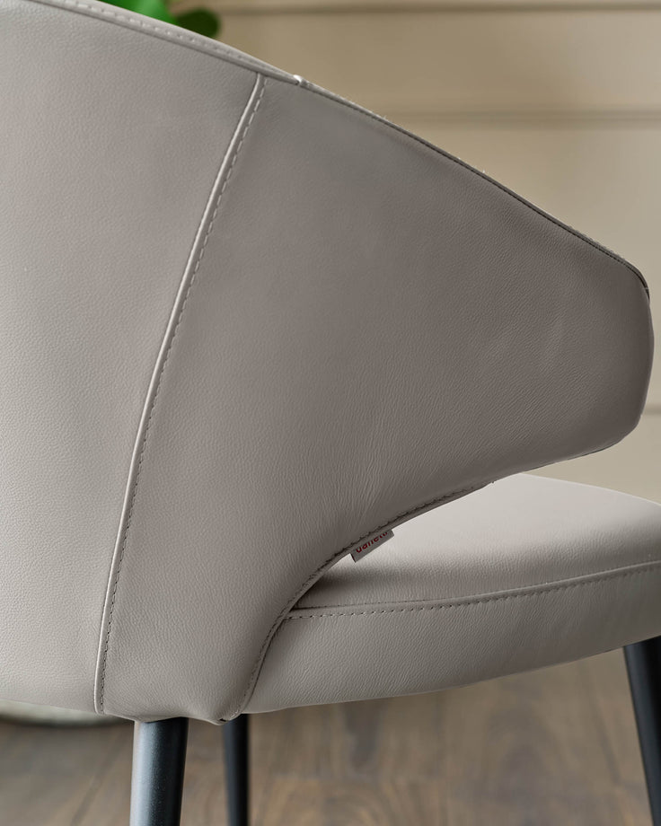 Light grey leather dining chair, close-up of curved backrest and metal leg detail.