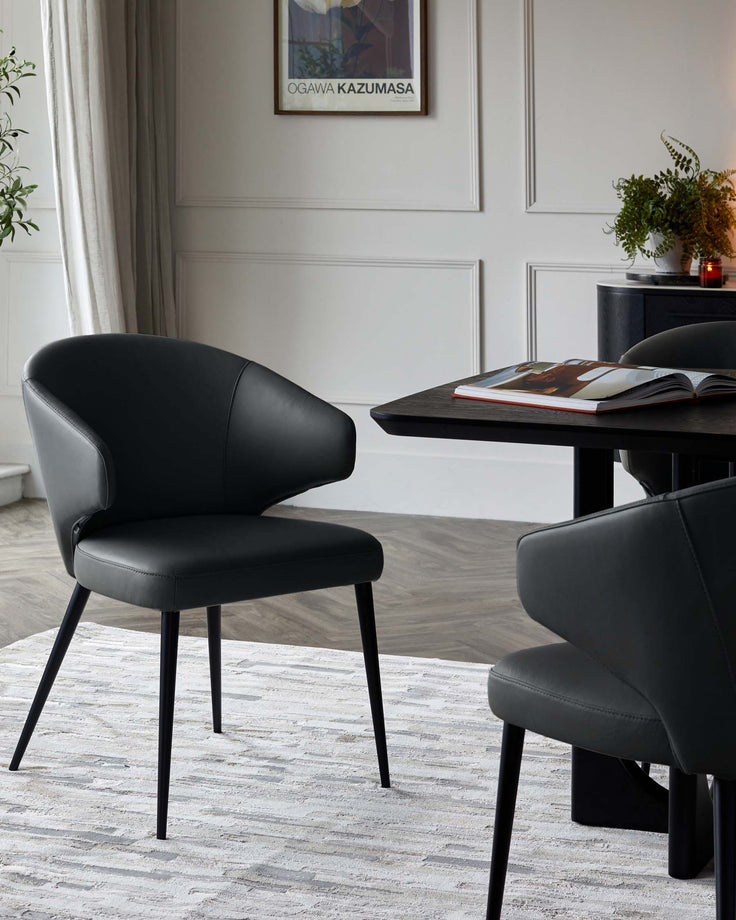 Landon black leather dining chair with curved backrest and black metal legs, shown at a dining table in a modern room setting.
