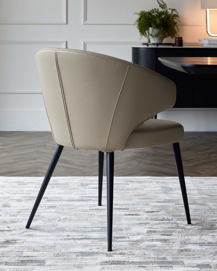 Sleek cream leather chair with a curved back and black tapered legs, set against a textured rug and minimalist decor.