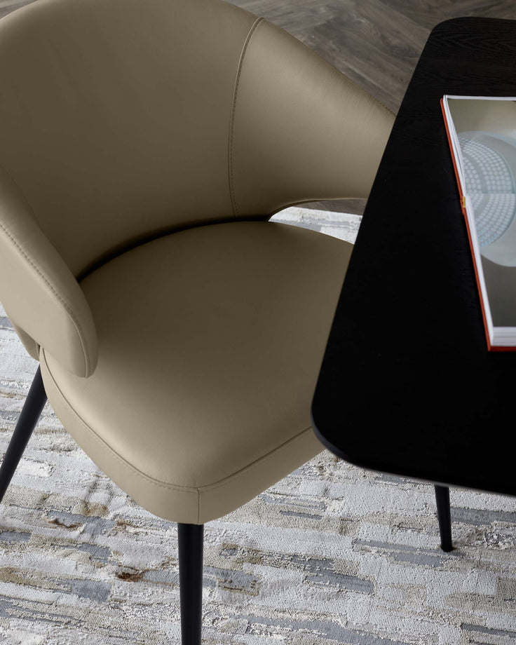 A sleek, modern beige upholstered chair with black legs, alongside a dark table partially visible with a magazine on top.