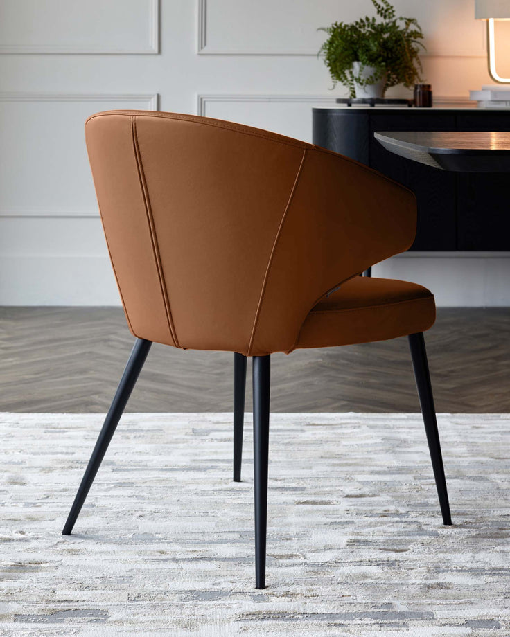 Tan leather dining chair with curved back, black tapered legs, shown from rear angle in modern room setting.
