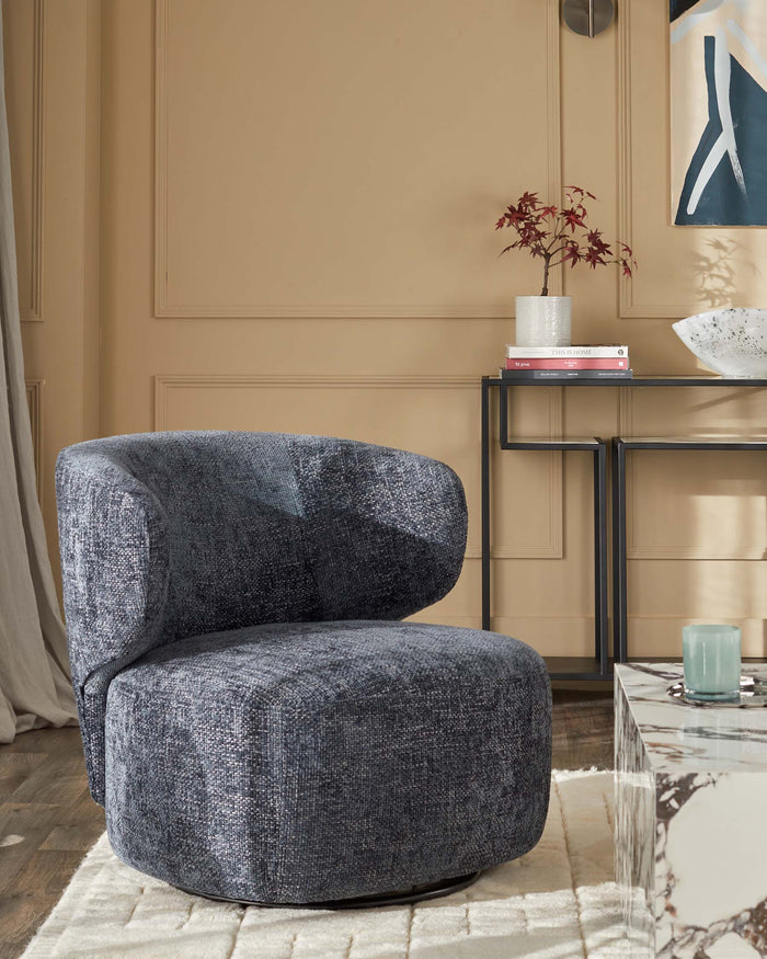 A blue textured swivel chair sits on a cream rug, with a console table, marble side table, and artwork nearby.