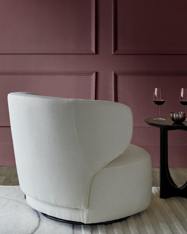 Cream swivel chair next to round black table with wine glasses, against a panelled maroon wall.
