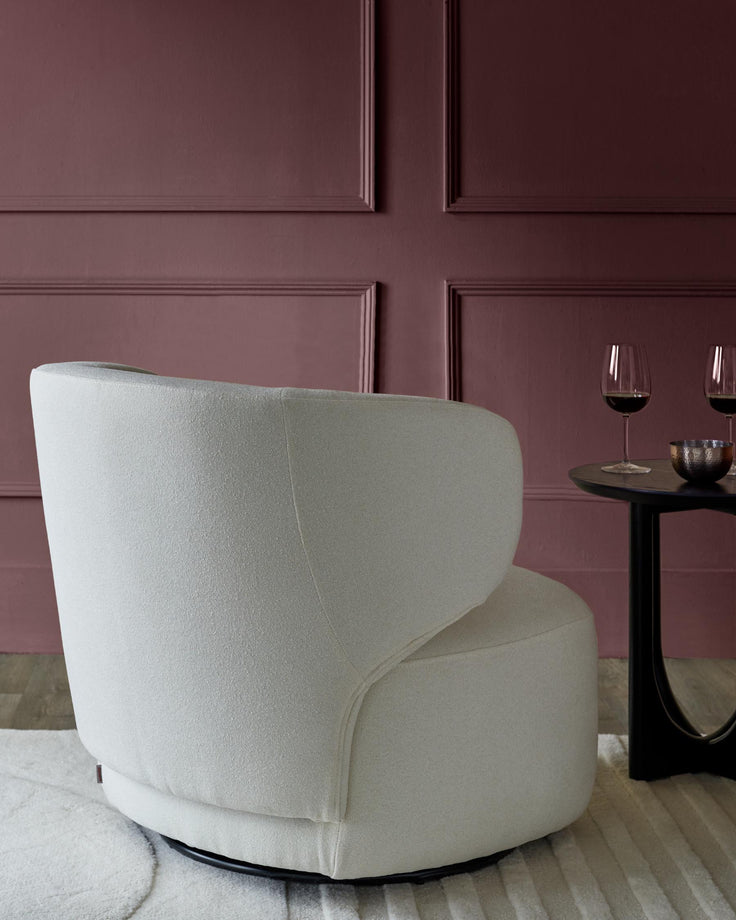 Cream swivel chair next to round black table with wine glasses, against a panelled maroon wall.