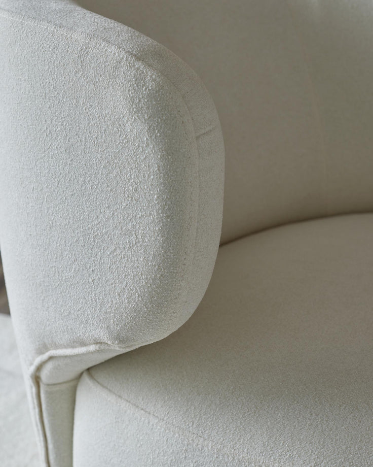 Close-up of a cream, textured armchair showing the rounded arm and part of the seat, exuding comfort and quality.