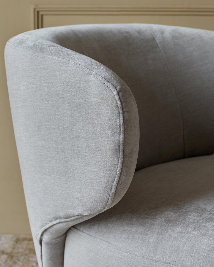 Close-up of a light grey upholstered armchair, showcasing the rounded arm and textured fabric.