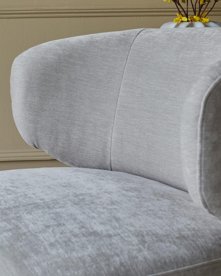 Close up of a stylish light grey armchair. Its curved shape and plush fabric suggest comfort and modern design.