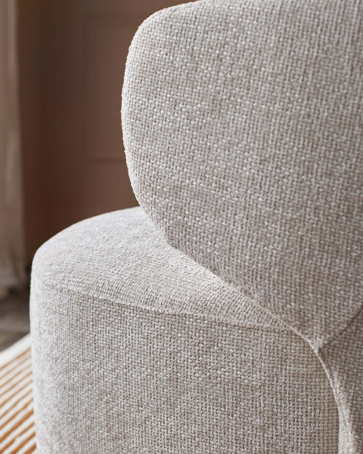 Close-up of a beige textured armchair, showcasing its soft, inviting fabric and curved design. Cosy comfort for your living room.