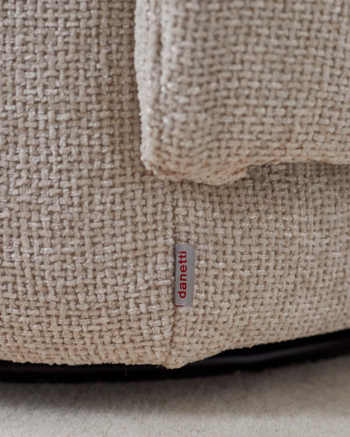 Close-up of a light brown textured sofa with a Danetti label, showcasing its fabric and construction.
