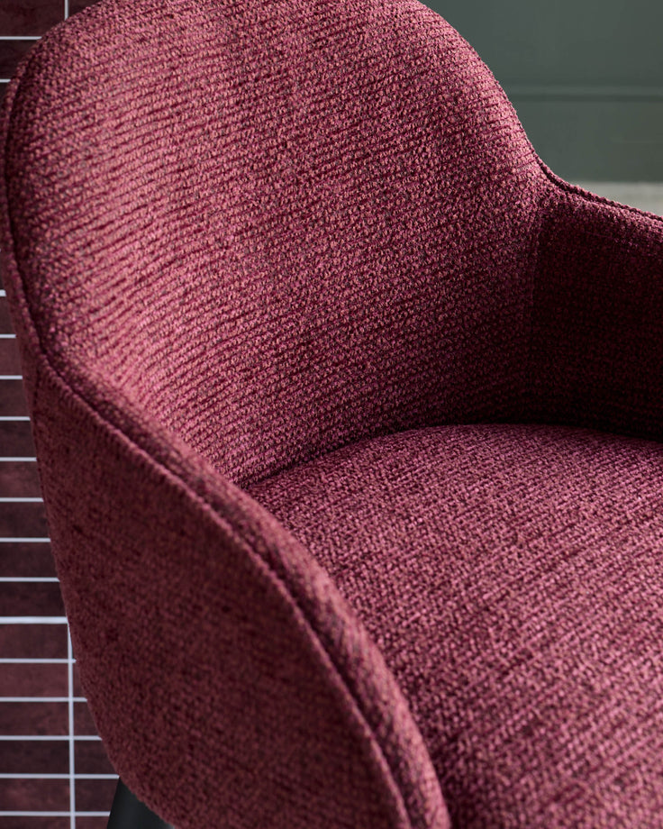 Close-up of a stylish, crimson upholstered chair with a textured fabric finish, exuding comfort and modern design.