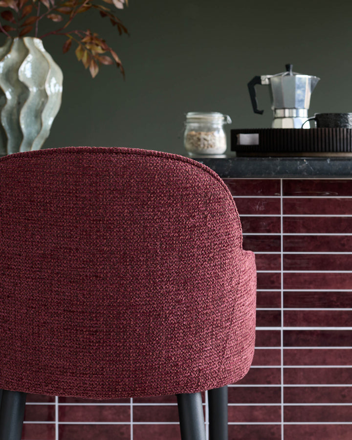 Burgundy chair in front of a kitchen island with accessories such as coffee maker and a jar of oats.