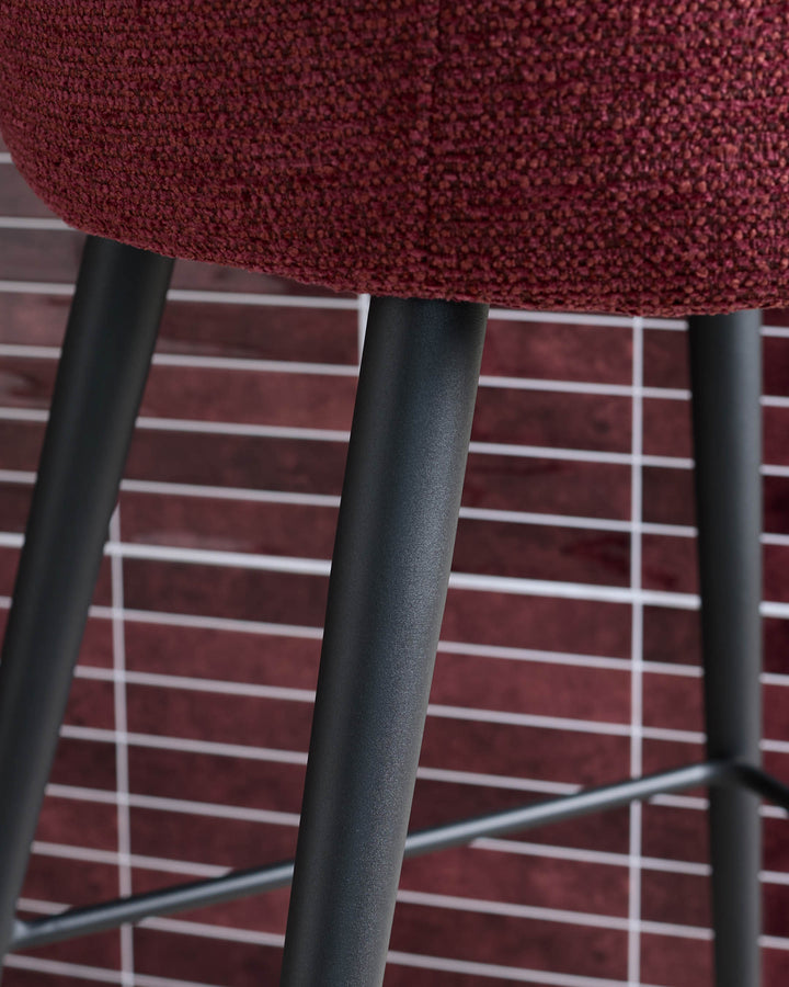 Close-up of a stylish bar stool with a burgundy seat and sleek, dark metal legs against a tiled backdrop.