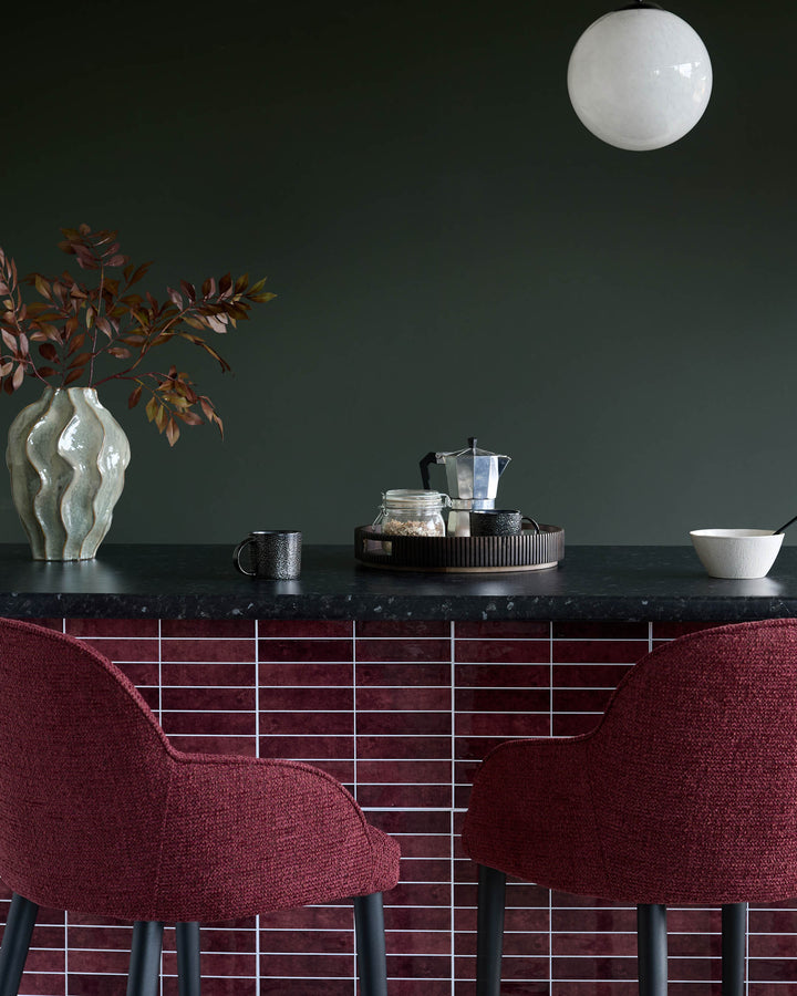 Contemporary kitchen counter with bar stools, mugs, a vase and a coffee maker.