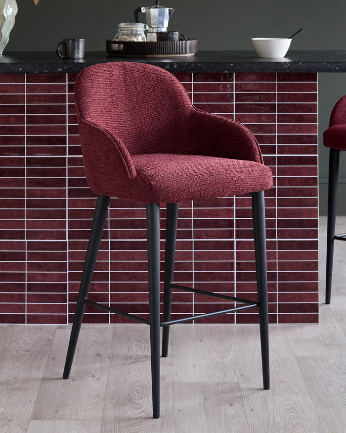 A burgundy fabric bar stool with black legs sits in front of a tiled splashback and breakfast bar.