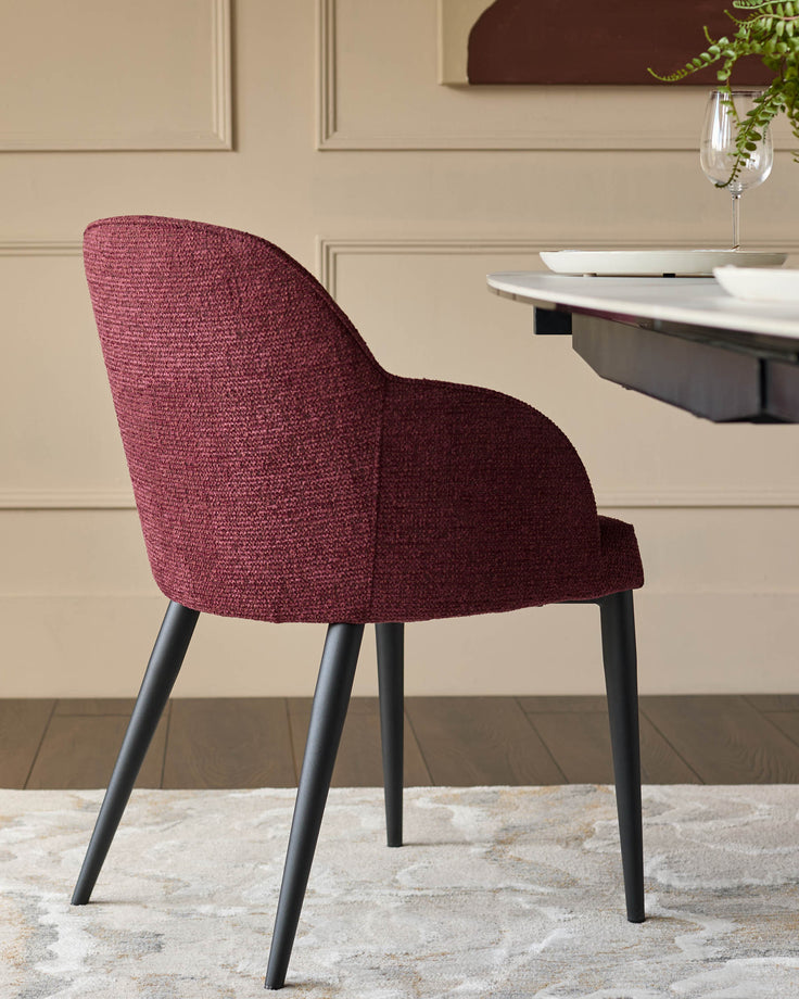 A stylish, fabric dining chair in claret with black legs sits beside a dining table on a patterned rug.