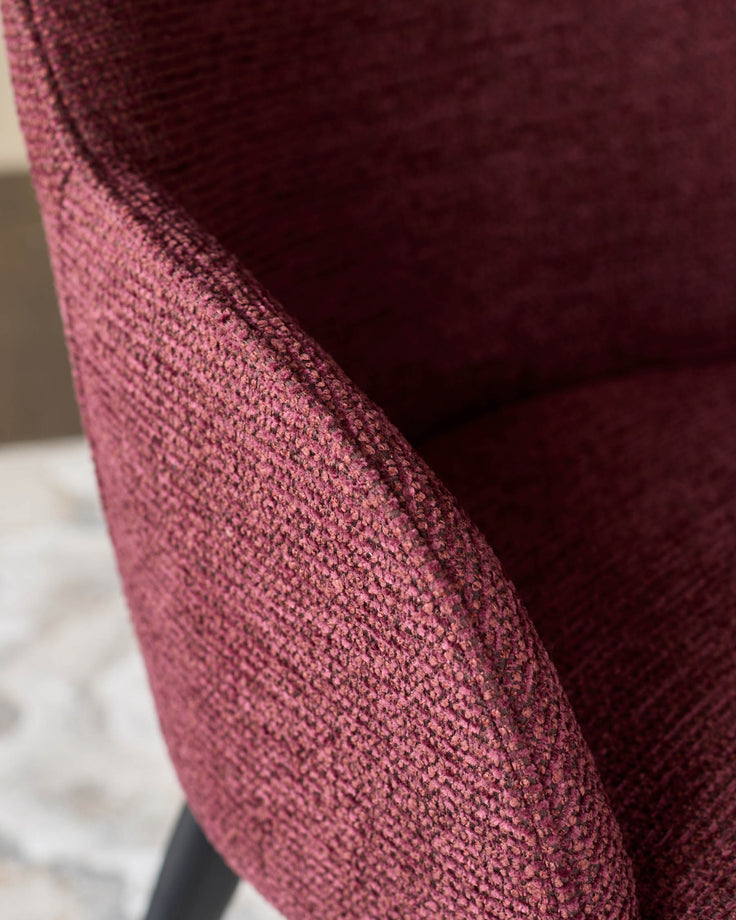 Close-up of a claret-coloured, upholstered chair, showcasing the fabric's texture and the curve of the chair's design.