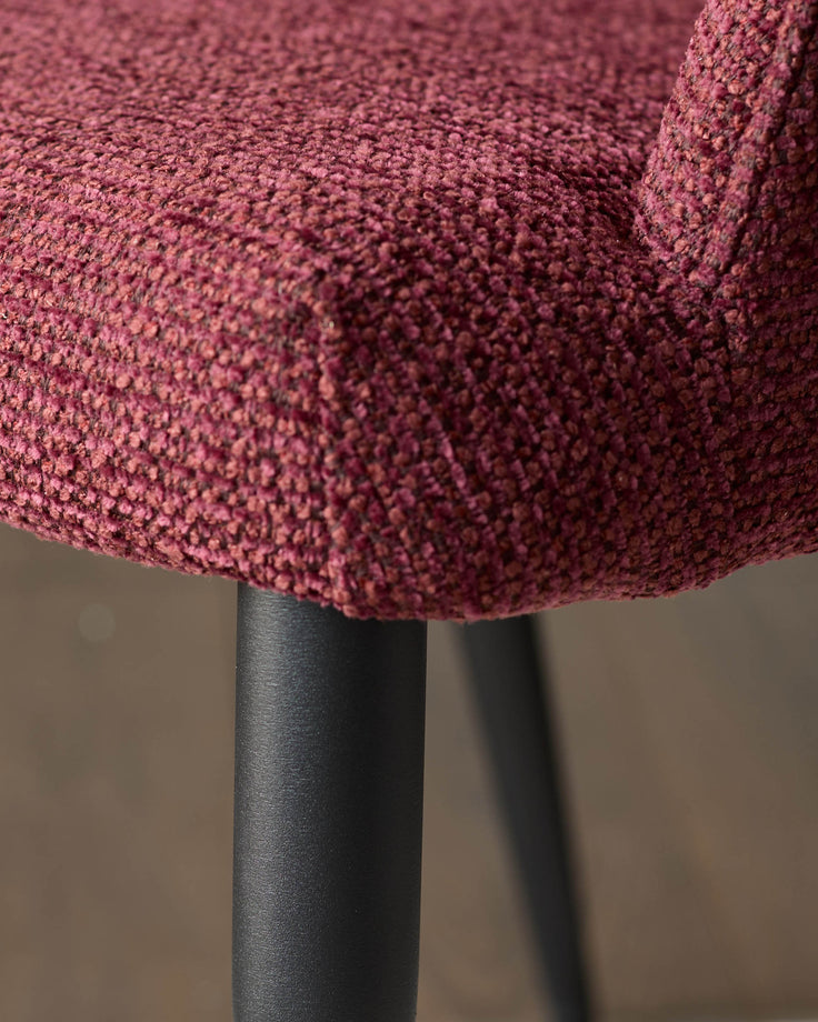 Close-up of a plush, burgundy chair seat and sleek, black legs. Modern comfort meets minimalist design.