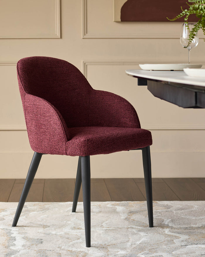 A stylish burgundy fabric chair with black legs sits on a patterned rug, next to a dining table.