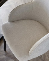 Light grey boucle dining chair with curved backrest and seat, viewed from above at an angle, showing upholstered details and dark legs.