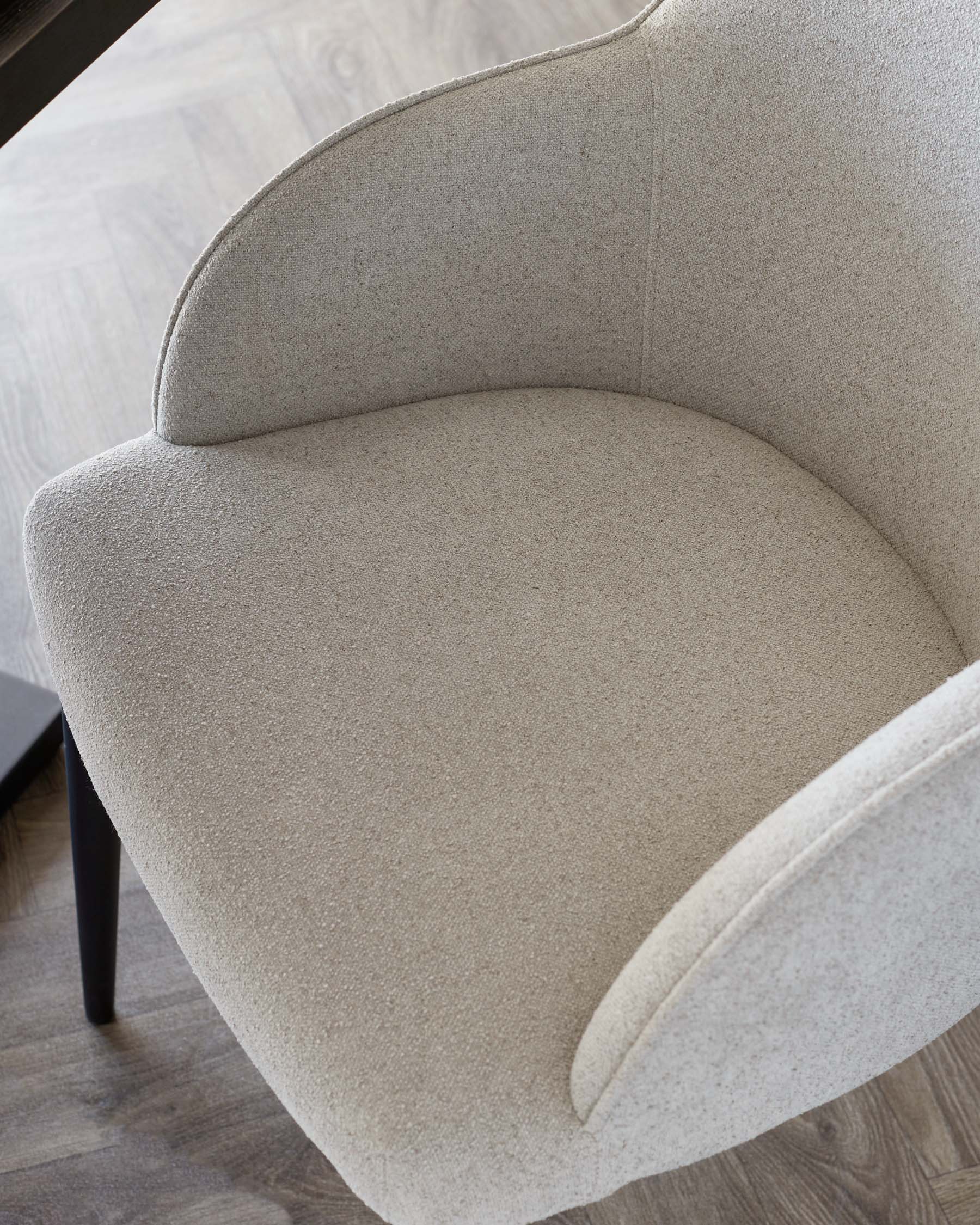 Light grey boucle dining chair with curved backrest and seat, viewed from above at an angle, showing upholstered details and dark legs.