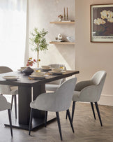 Pair of light grey boucle dining chairs with black tapered legs, shown at a modern dining table in a styled room setting.