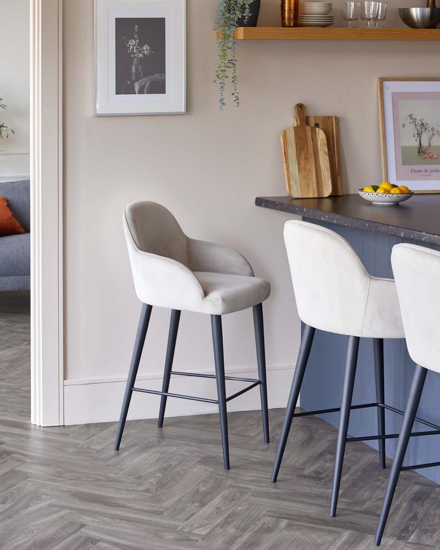 Modern bar stools with elegant light grey upholstery and slim black metal legs, positioned at a kitchen counter with a dark surface.