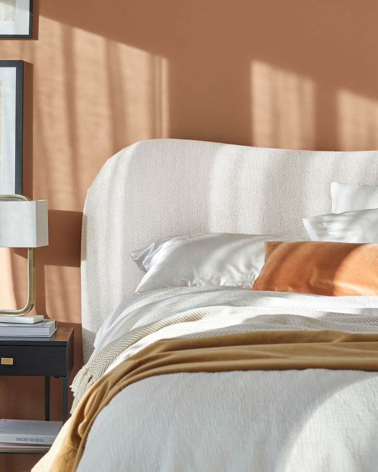 Soft, rounded bed frame with a textured headboard, layered bedding, and a sleek nightstand with a modern lamp.