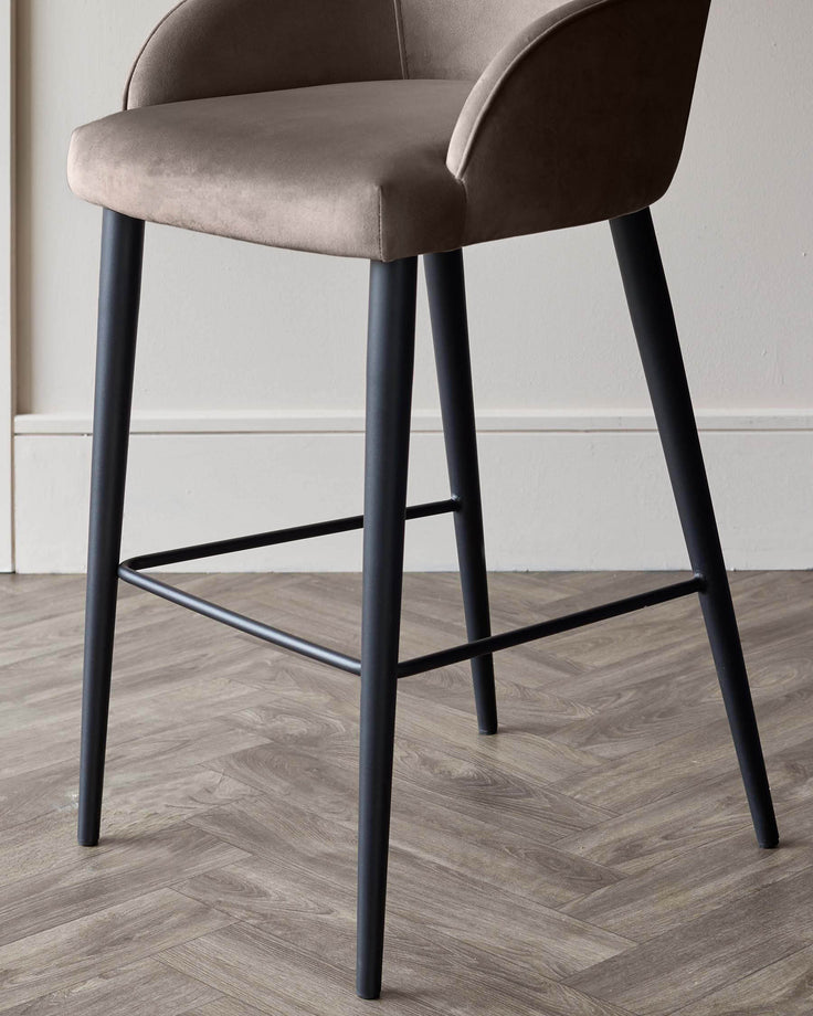Lani bar stool in mocha velvet with black wooden legs and footrest, shown at an angle on herringbone wood flooring.
